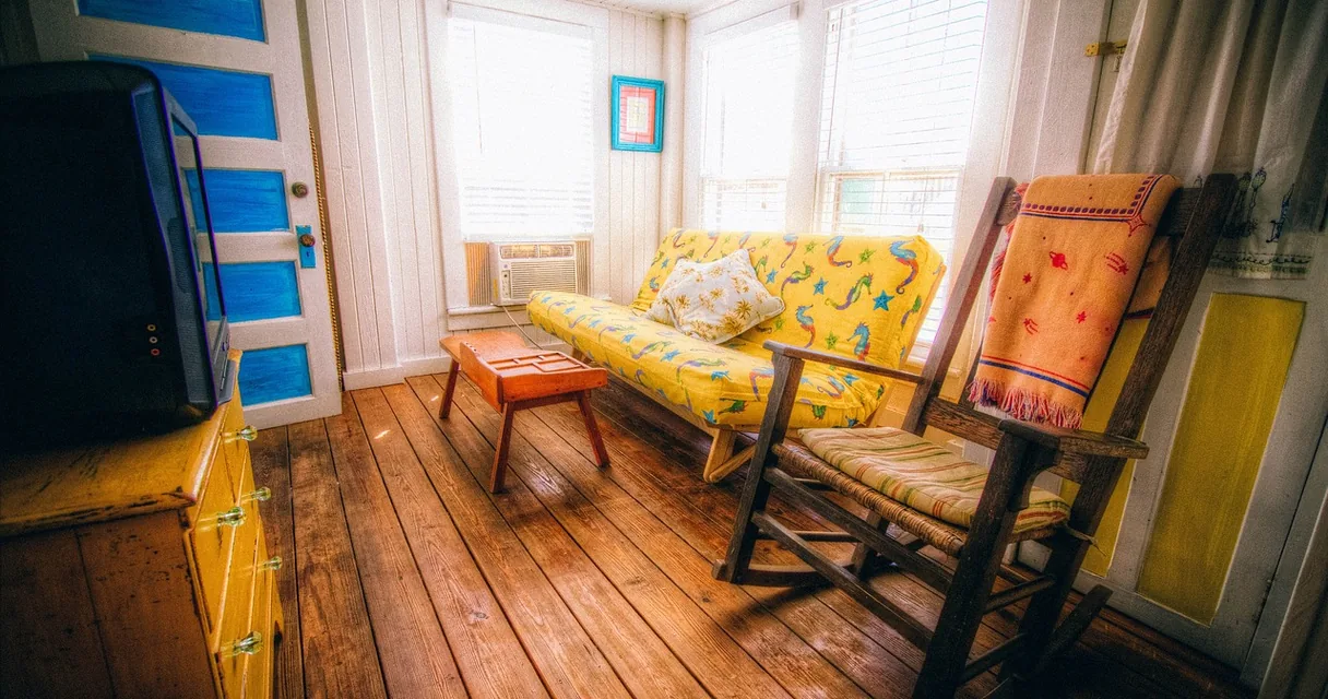 Sala com sofá amarelo, cadeira e televisão antiga sobre uma cômoda, ambiente para uma maratona de séries